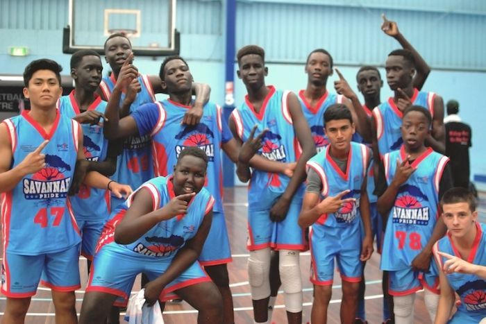 A group of teenagers post with "number one" symbol with their hands while wearing basketball uniforms